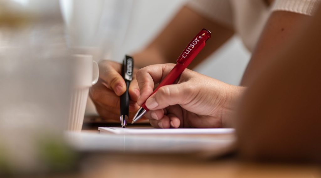 Kaksi kättä kirjoittamassa kynillä paperille.