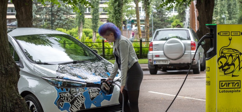 Ihminen lataamassa sähköautoa parkkipaikalla.