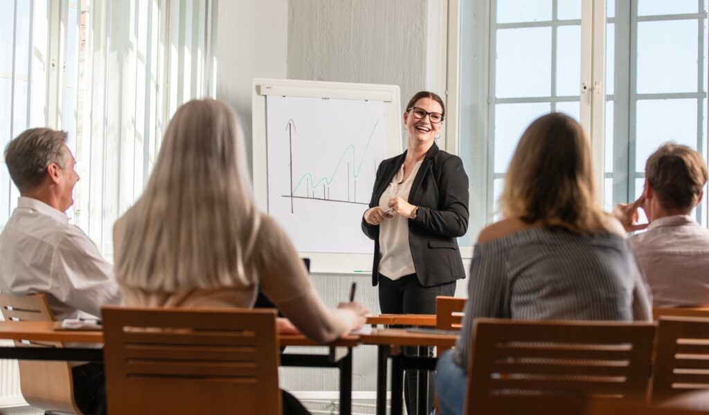 Neuvomme yritysrahoituksen hankinnassa. Kuvassa nainen fläppitaulun edessä puhumassa neljälle ihmiselle.