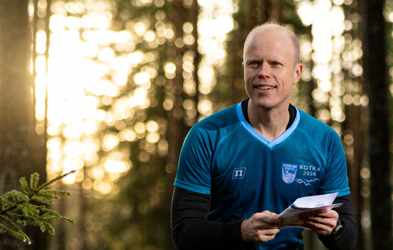 Jukka Tani suunnistamassa metsässä. Taustalla auringonlasku puiden välissä.