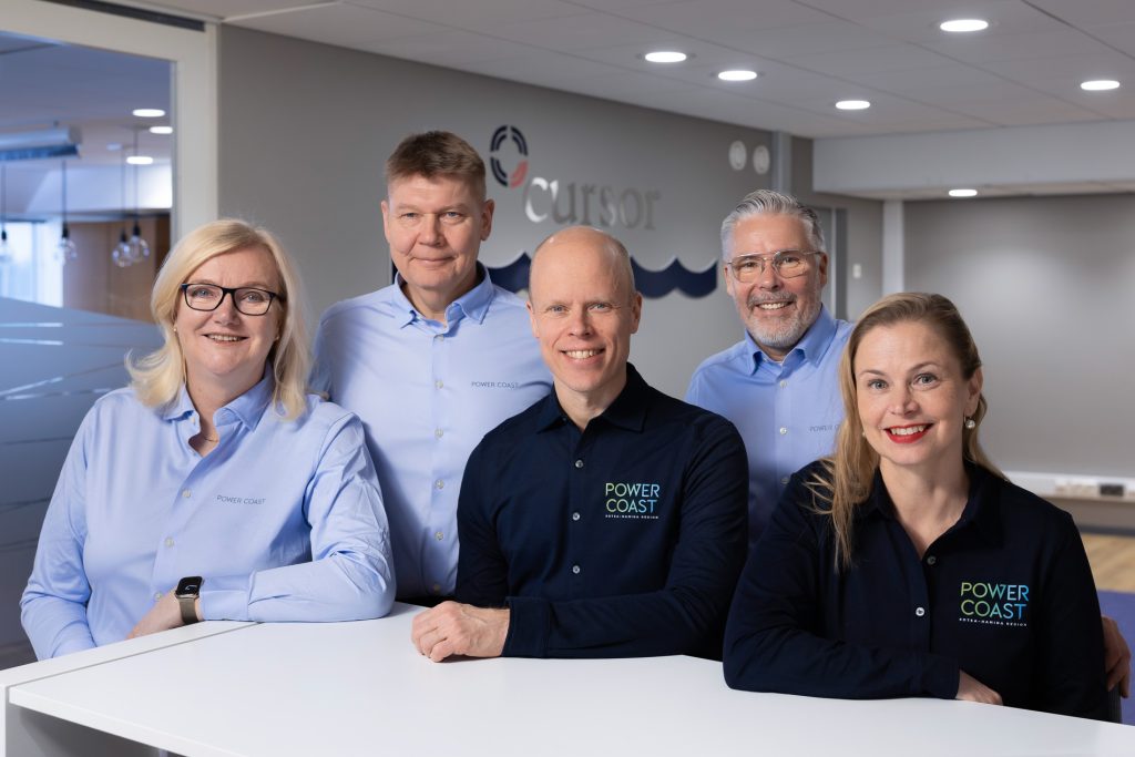 Cursorin Power Coast -tiimin yhteiskuva, jossa viisi henkilöä istuu vierekkäin ja katsoo kameraan.